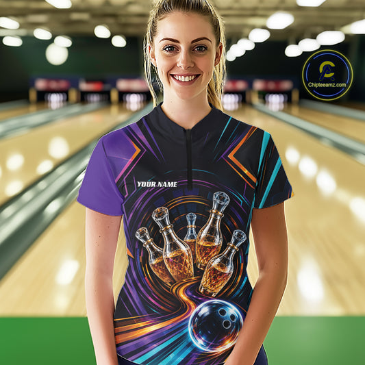 A woman stands in a bowling alley wearing a custom short-sleeve bowling shirt with a purple, black, and blue graphic design featuring bowling pins that resemble wine bottles and ball.