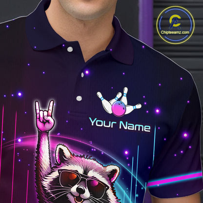 A close-up of a person wearing a dark navy polo shirt with a colorful custom graphic print. The print features a raccoon wearing sunglasses and making a rock-on gesture, along with bowling pins and the text 'Your Name' and a bowling ball.