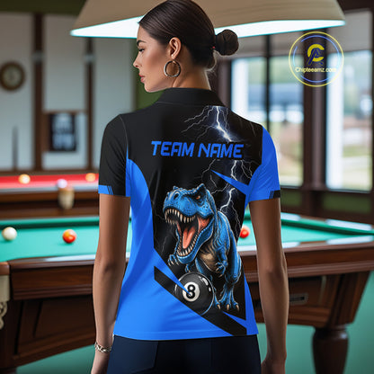 A woman stands in a billiards room wearing a custom short-sleeve collared shirt, viewed from the back. The shirt features a black upper back with a blue 'TEAM NAME' text and a graphic of a roaring blue T-Rex under lightning, with a blue and black lower back showing a 3-ball design.