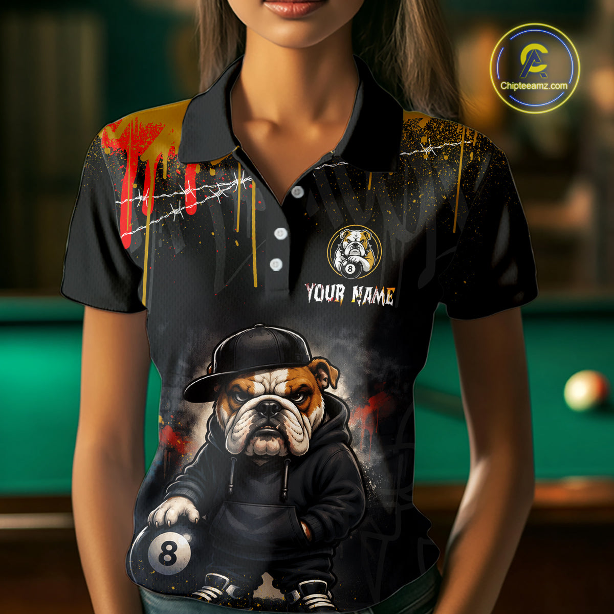 A front view of a custom blue and yellow billiards polo shirt worn by a female model . The shirt features  a cartoon hip hop bulldog and an 8-ball on the front. A 'YOUR NAME' text placeholder . The background is a blurred billiards room with a green pool table.