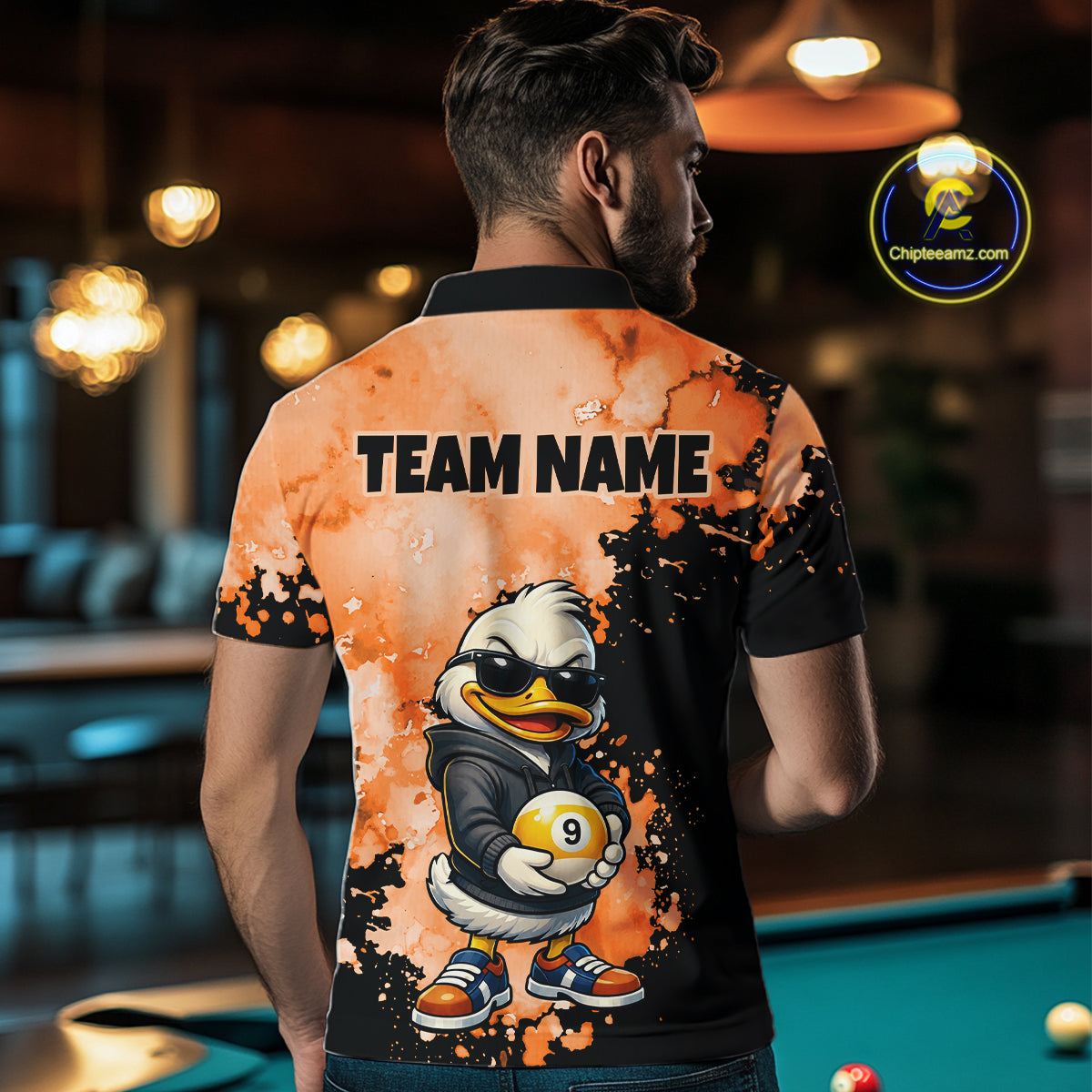A man viewed from behind wearing a short-sleeve polo shirt with a custom graphic design. The shirt features a black and orange splatter background with a cartoon duck character wearing sunglasses and holding a billiard ball, and the text 'TEAM NAME' printed across the upper back.