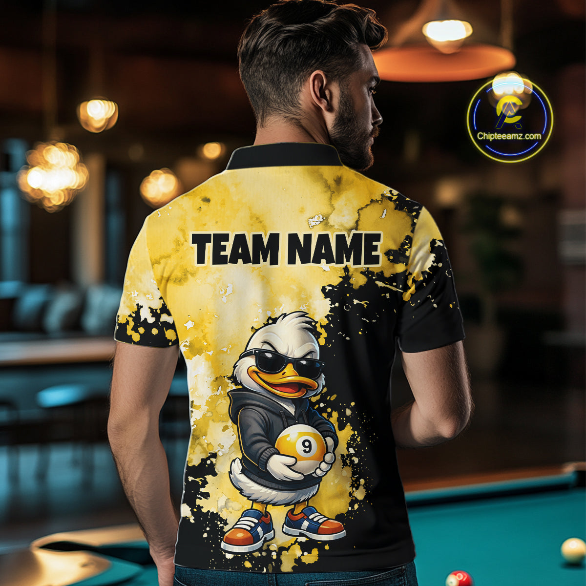 A man viewed from behind wearing a short-sleeve collared shirt with a black and yellow graphic design. The back of the shirt features the text 'TEAM NAME' above a cartoon duck character holding a billiard ball.