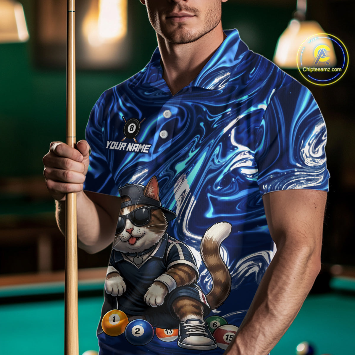 Man wearing a blue shirt with a cat design holding a pool cue on a pool table.
