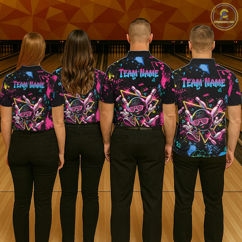Four people standing with their backs to the camera in a bowling alley, wearing matching black short-sleeve bowling shirts with a colorful neon bowling pin and ball graphic on the back, along with black pants. The shirts have 'TEAM NAME' printed in white on the left shoulder area.