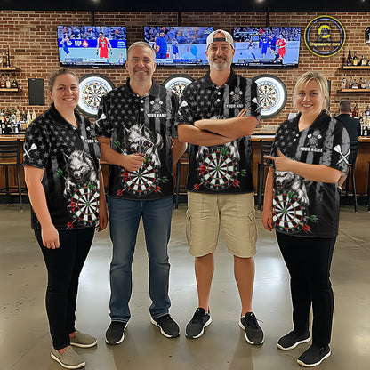 Four people standing together in a bar wearing matching black short-sleeve polo shirts with a white star pattern, a large dartboard graphic on the front. The background shows a brick wall, bar shelves, and mounted sports screens.