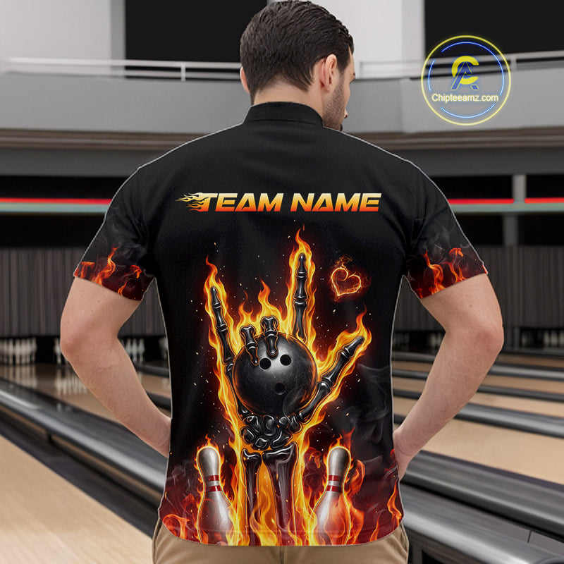 A man viewed from behind wearing a black short-sleeve bowling shirt with a large back graphic showing a skeleton hand holding a bowling ball surrounded by flames, with bowling pins and the text 'TEAM NAME' on the back. Bowling lanes are visible in the background.