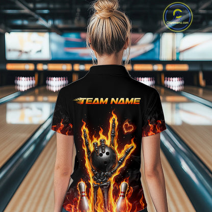 A woman viewed from behind wearing a black short-sleeve bowling shirt with a large graphic print of a flaming bowling ball and pins, with 'TEAM NAME' printed across the upper back. The background shows a blurred bowling alley.