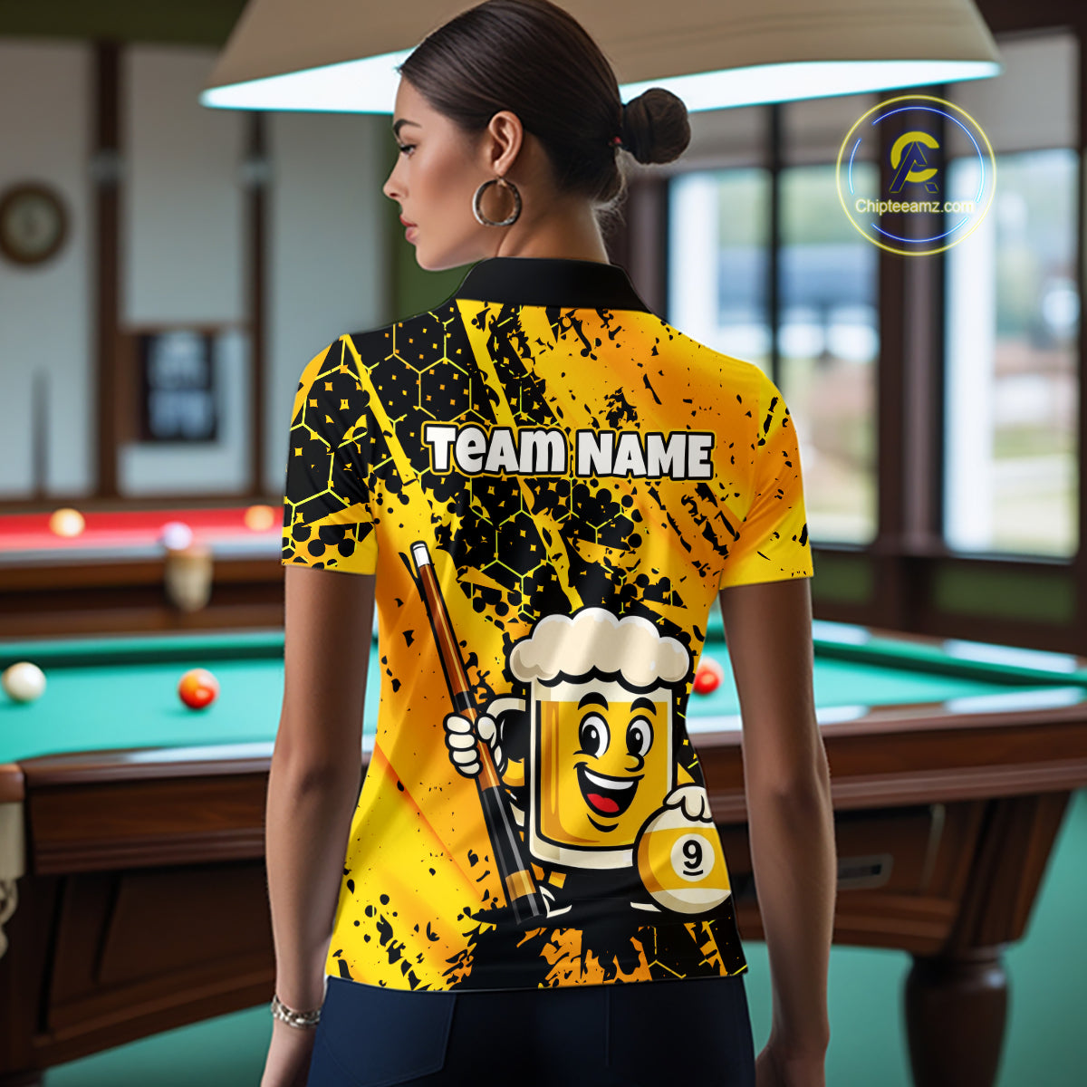 Woman wearing a bright yellow billiards polo with black splatter graphics, custom “TEAM NAME” text, and a smiling beer mug mascot holding a pool cue.