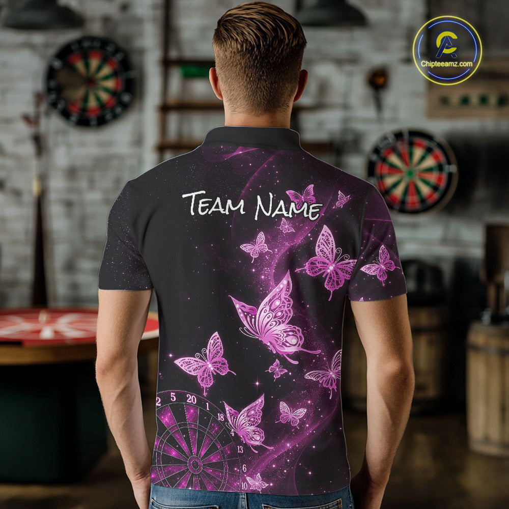 A man viewed from behind wearing a black short-sleeve polo shirt with a purple and pink butterfly print, white 'TEAM NAME' text across the upper back, and a dartboard graphic near the lower left. The shirt is shown in a blurred indoor setting with dartboards in the background.