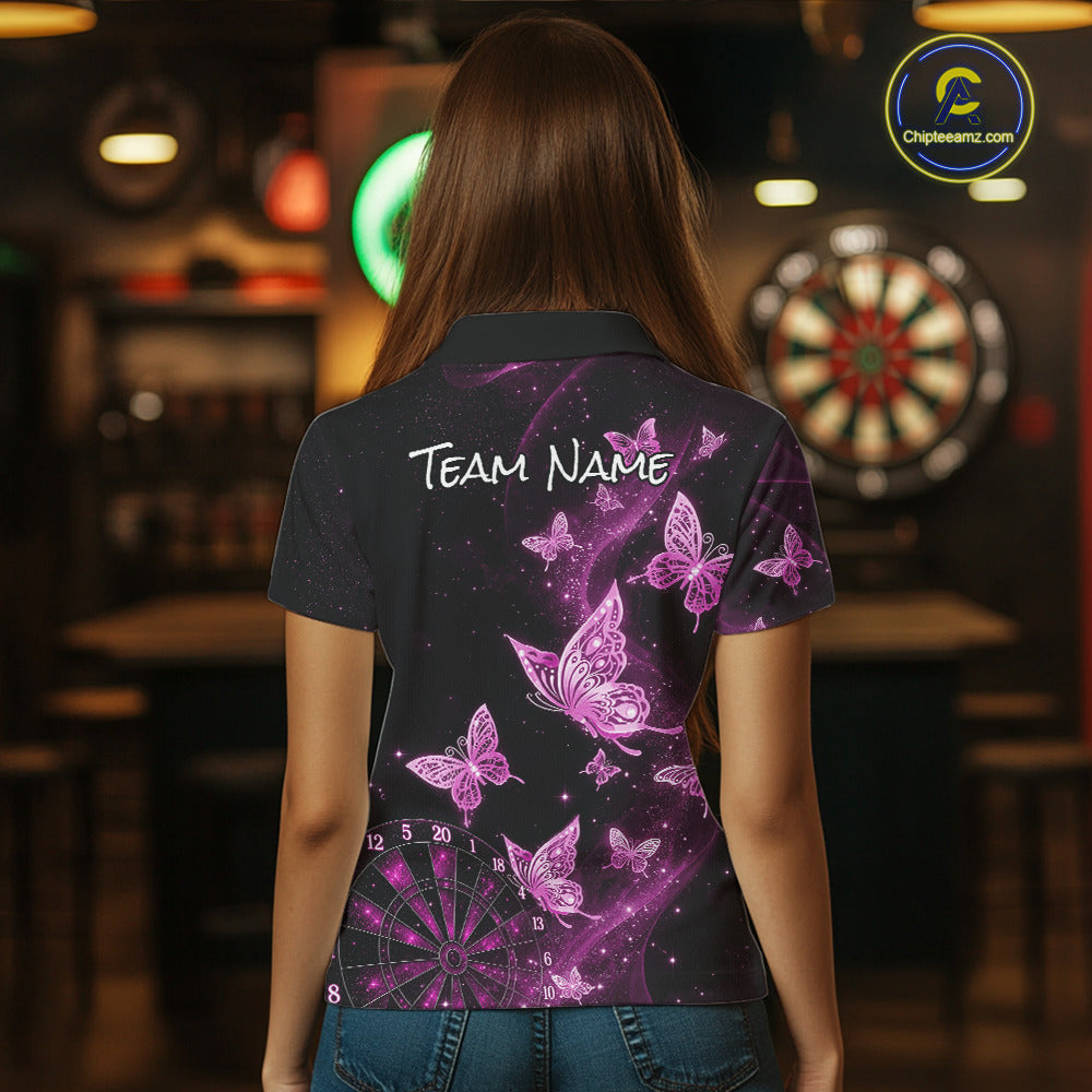 A woman viewed from behind wearing a dark short-sleeve polo shirt with a purple and pink butterfly and dartboard print, standing in a dimly lit bar environment.