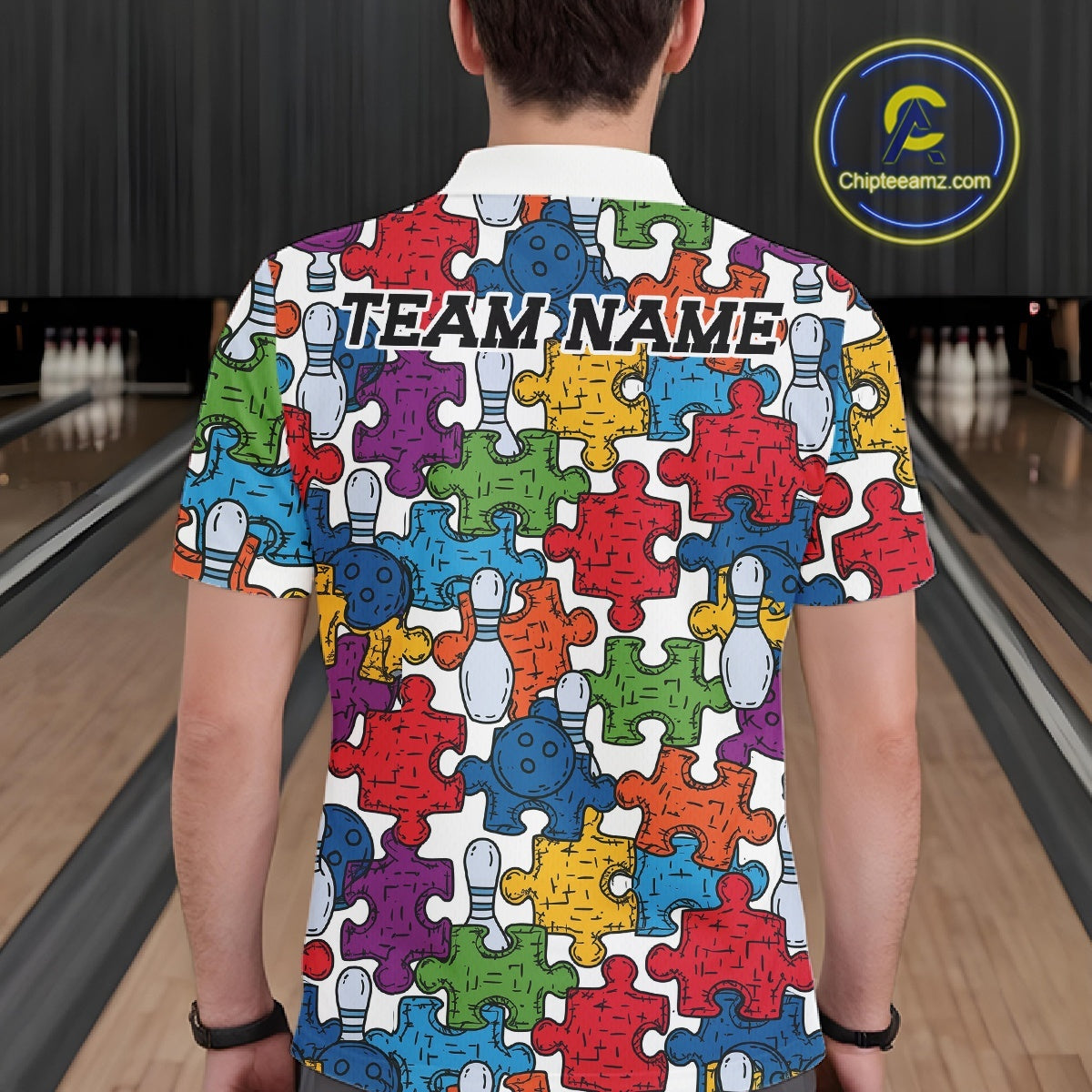A man viewed from behind wearing a white short-sleeve bowling-themed t-shirt with a colorful jigsaw puzzle pattern of bowling pins and puzzle pieces. The shirt features 'TEAM NAME' printed across the upper back.
