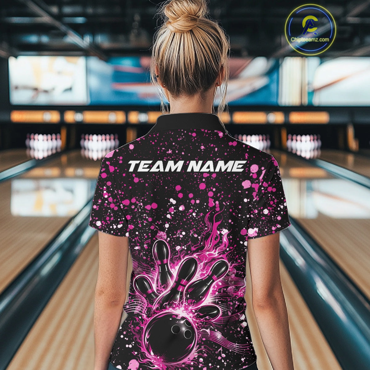 Back view of a female model in a black bowling polo shirt displaying fiery bowling artwork with pink paint accents.