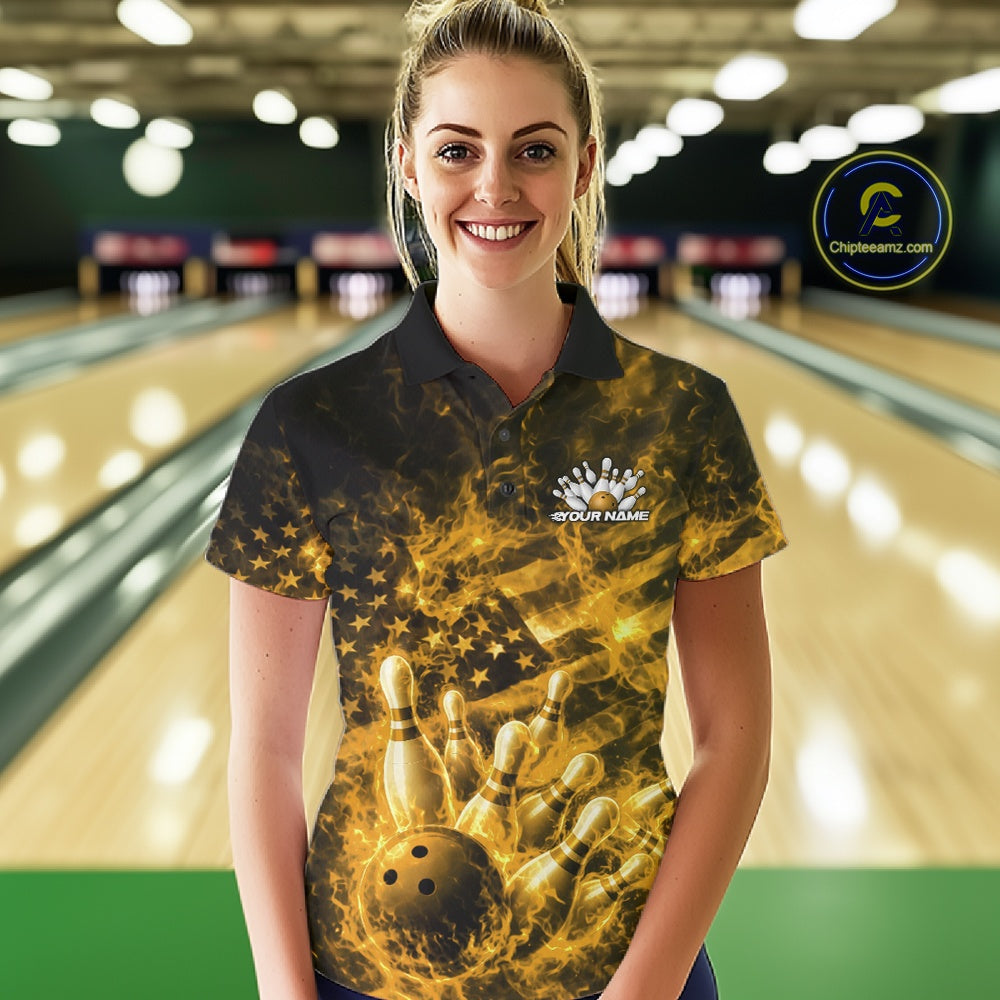 Female model in a bowling center wearing a black and yellow polo decorated with fiery patriotic bowling artwork.
