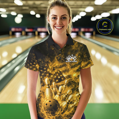 Female model in a bowling center wearing a black and yellow polo decorated with fiery patriotic bowling artwork.