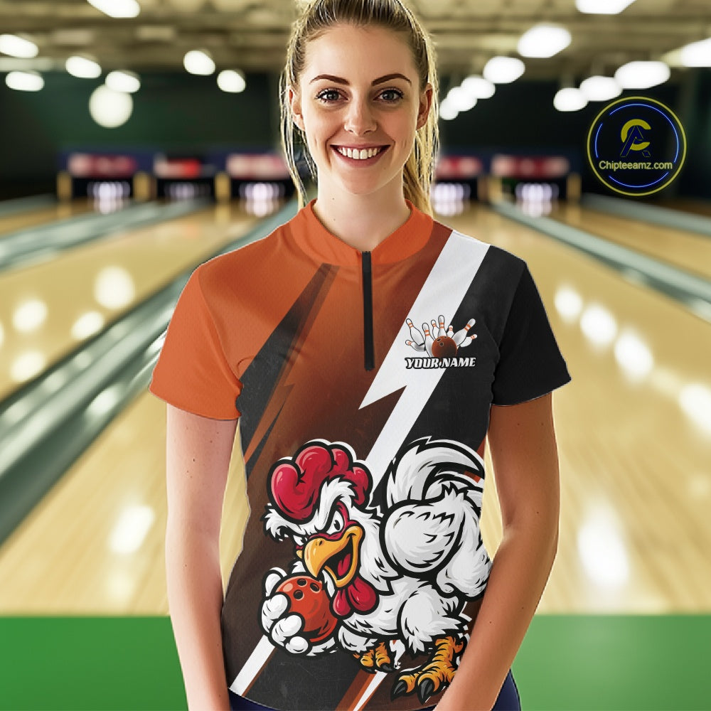 A woman standing in a bowling alley wearing a custom short-sleeve bowling jersey with an orange, black, and white design featuring a cartoon rooster mascot and the text 'Your Name'.