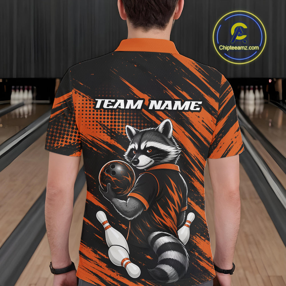 A person viewed from behind wearing a short-sleeve polo collared shirt in a bowling alley. The shirt has an orange and black brush-stroke design with a raccoon holding a bowling ball and pins, and the text 'TEAM NAME' across the upper back.