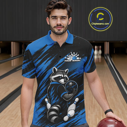A man wearing a custom short-sleeve bowling polo shirt with a raccoon graphic, standing in a bowling alley. The shirt features a black and blue brush-stroke pattern with a raccoon holding a bowling ball and pins, and a customizable name print on the chest.