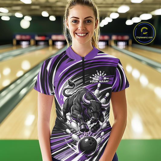 A woman stands in a bowling alley wearing a short-sleeve quarter zip  bowling jersey with a purple, black, and white bull graphic and the text 'YOUR NAME'.
