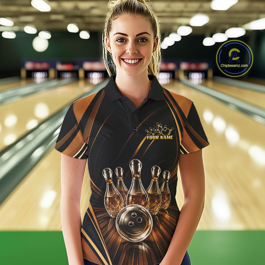 A woman stands in a bowling alley wearing a custom short-sleeve bowling polo shirt. The shirt features a black base with metallic gold and brown graphic stripes, a printed graphic of bowling pins that resemble wine bottles and a bowling ball, and 'YOUR NAME' printed in gold on the chest.