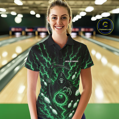 A woman stands in a bowling alley wearing a black short-sleeve polo shirt with a green grim reaper and bowling ball graphic. The shirt features the text 'YOUR NAME' on the chest