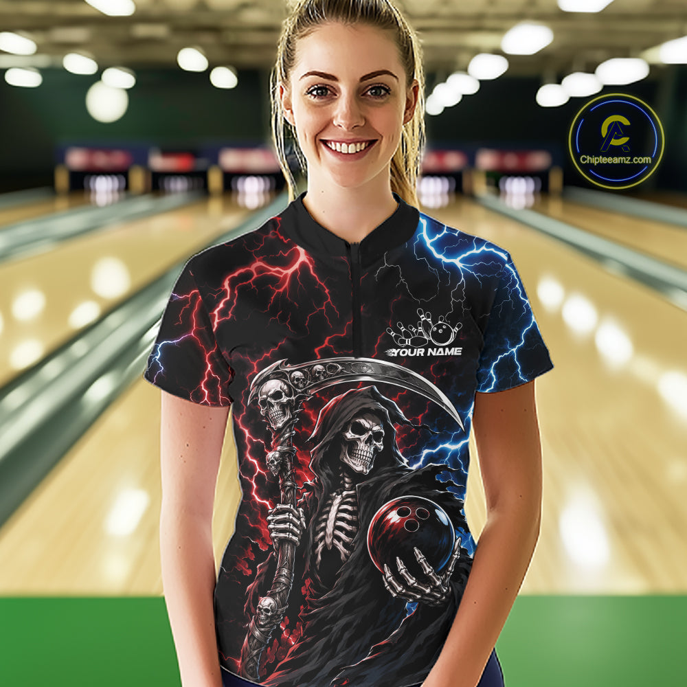 A woman wearing a black short-sleeve bowling shirt with a grim reaper graphic, red and blue lightning effects, and a bowling ball design, standing in a bowling alley. 