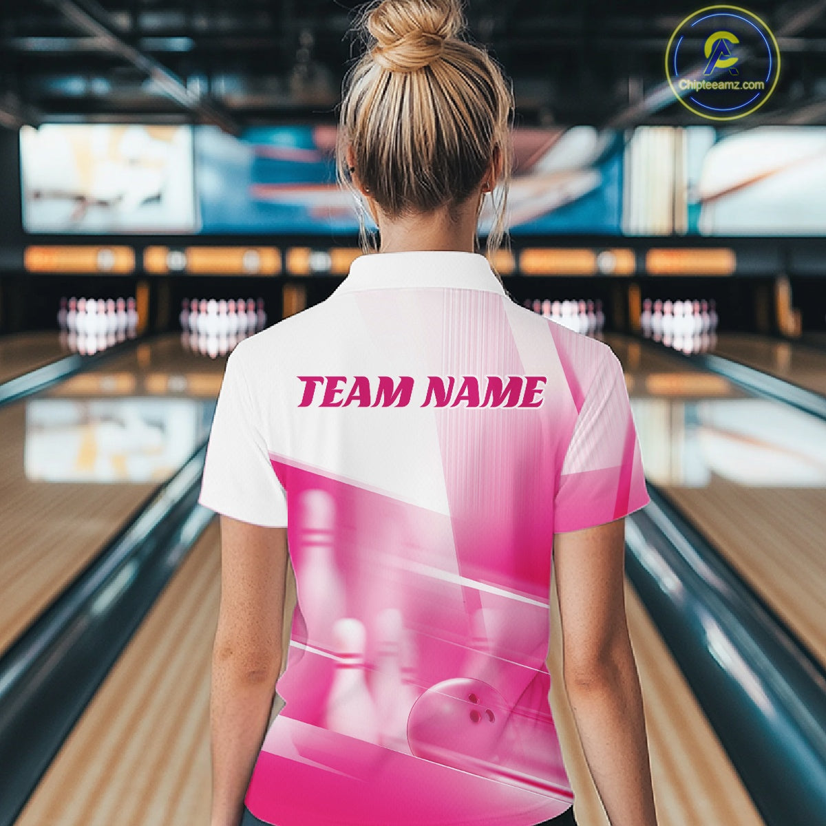 Back view of a female model in a bowling lane wearing a white and pink quarter zip shirt with bowling ball and pins over a pink geometric background.
