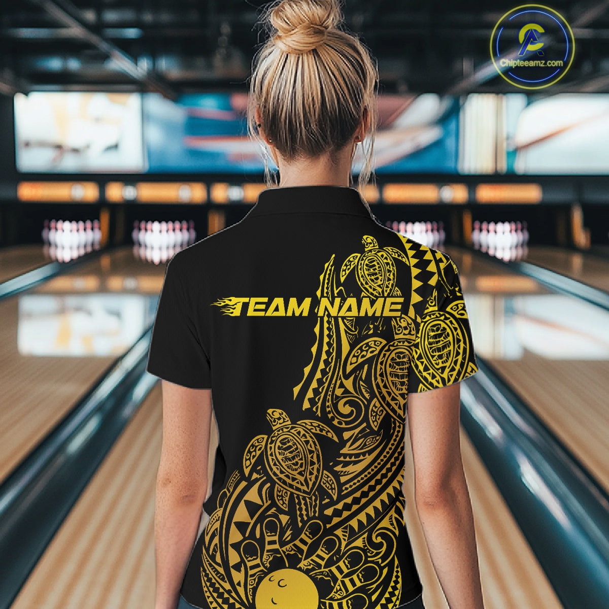 Back view of a female model in a black and gold bowling polo shirt displaying tribal bowling artwork and turtle pattern accents.