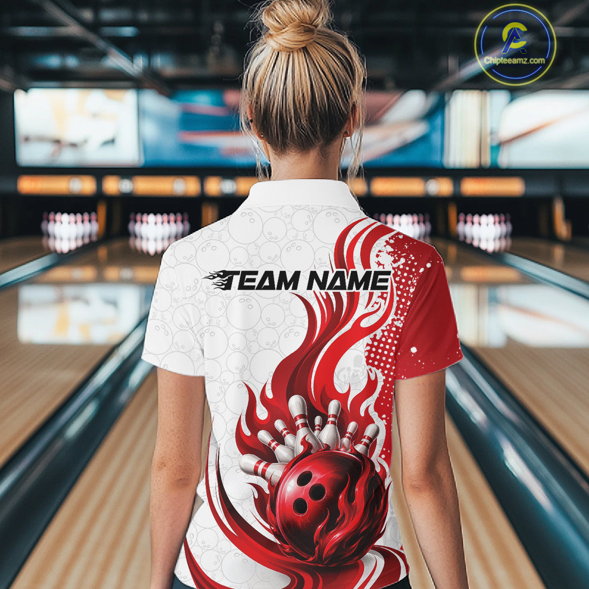 A woman viewed from behind wearing a white and red bowling-themed short-sleeve collared shirt with a flame and bowling ball graphic, standing in a bowling alley.