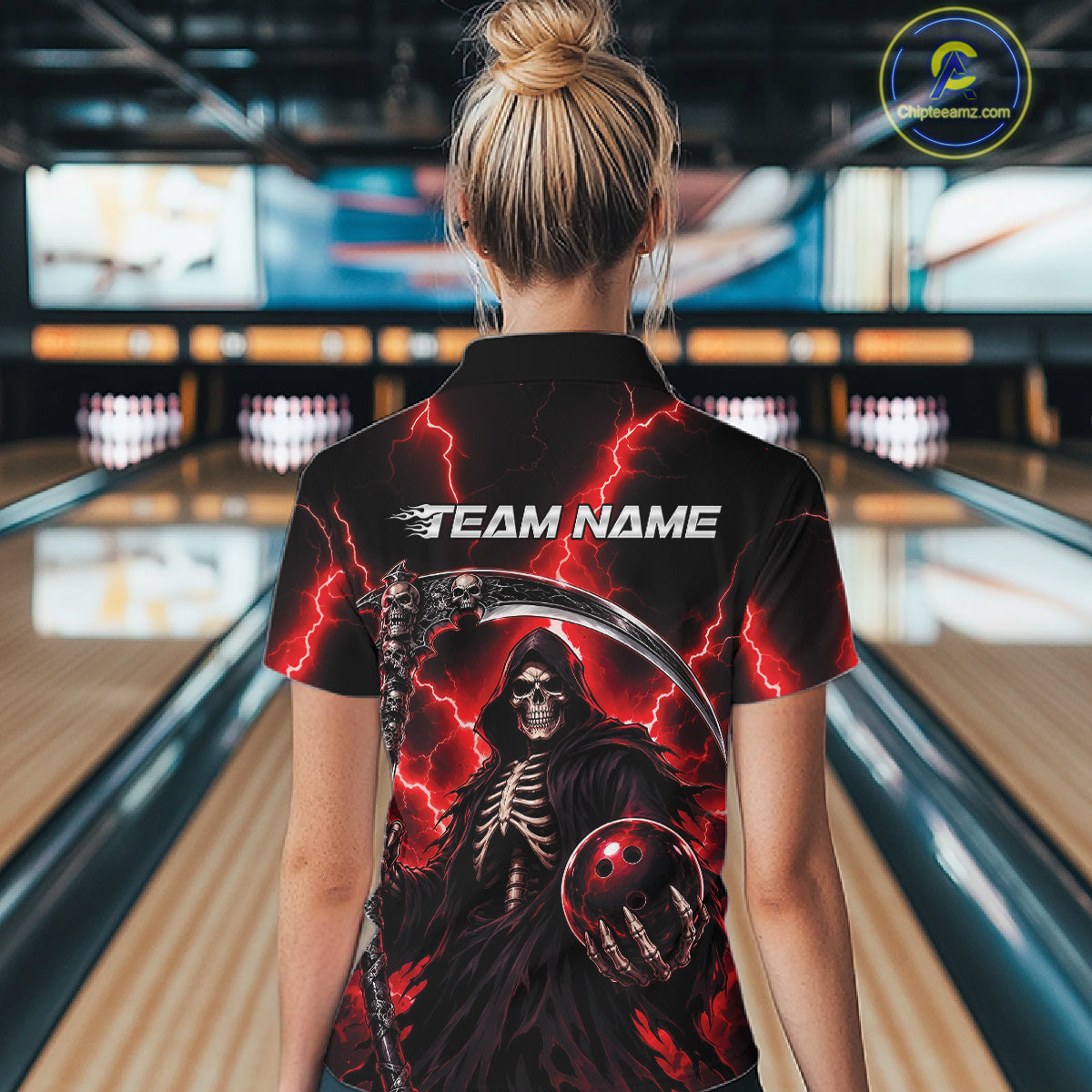 A woman viewed from behind wearing a black short-sleeve bowling shirt with a large grim reaper graphic, red lightning, and the text 'TEAM NAME' on the back. The background shows blurred bowling lanes in a bowling alley.