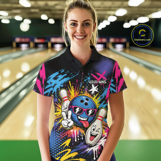 A woman stands in a bowling alley wearing a custom short-sleeve polo shirt with a colorful bowling-themed graphic print. The shirt features a blue bowling ball and white bowling pins in a graffiti-style design with pink, blue, yellow, and black splatter details.