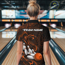 Load image into Gallery viewer, Female model standing in a bowling lane showing the back of a black and orange bowling polo shirt with a tribal flame bowling ball and pins graphic.