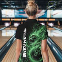Load image into Gallery viewer, Back view of a female model wearing a black bowling polo shirt in a bowling alley featuring a skull clutching a bowling ball surrounded by swirling green energy flames