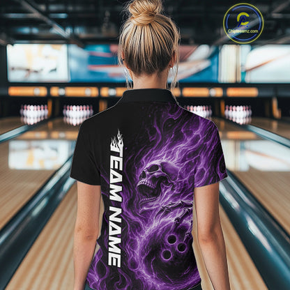 Back view of a female bowler in a bowling lane wearing a black bowling quarter-zip shirt with a purple energy-flame skull clutching a bowling ball