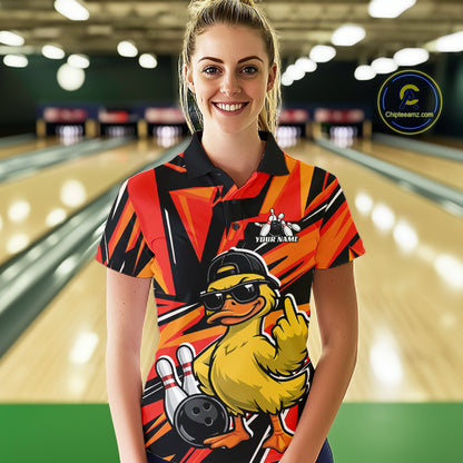 Female model at a bowling alley wearing a black and orange polo decorated with duck artwork, bowling pins, and geometric patterns.