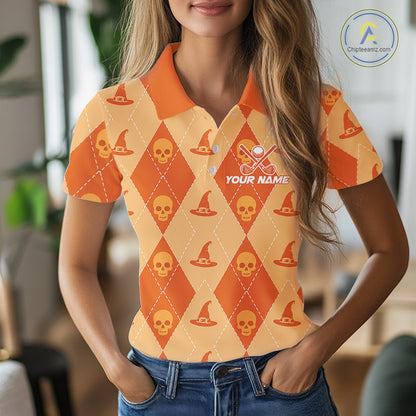 A woman wearing a short-sleeve polo shirt with an orange and yellow Halloween-themed argyle pattern featuring skulls, witch hats, and a customizable name patch. The background is a softly blurred indoor setting.